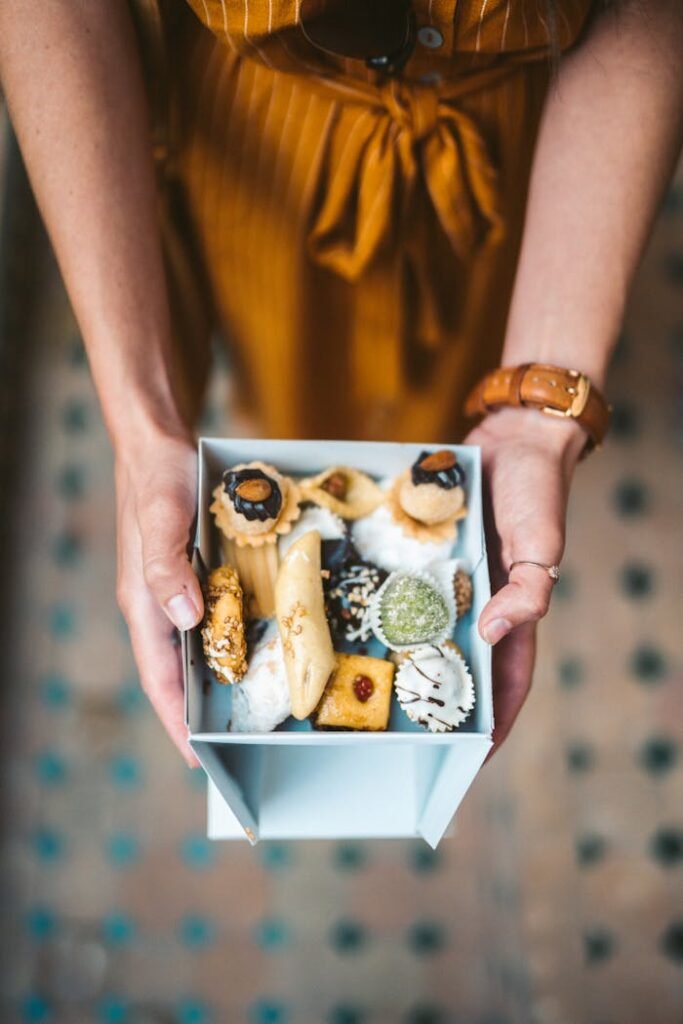 A top view of assorted Moroccan sweets in a decorative box held by hands, showcasing diverse treat styles.
